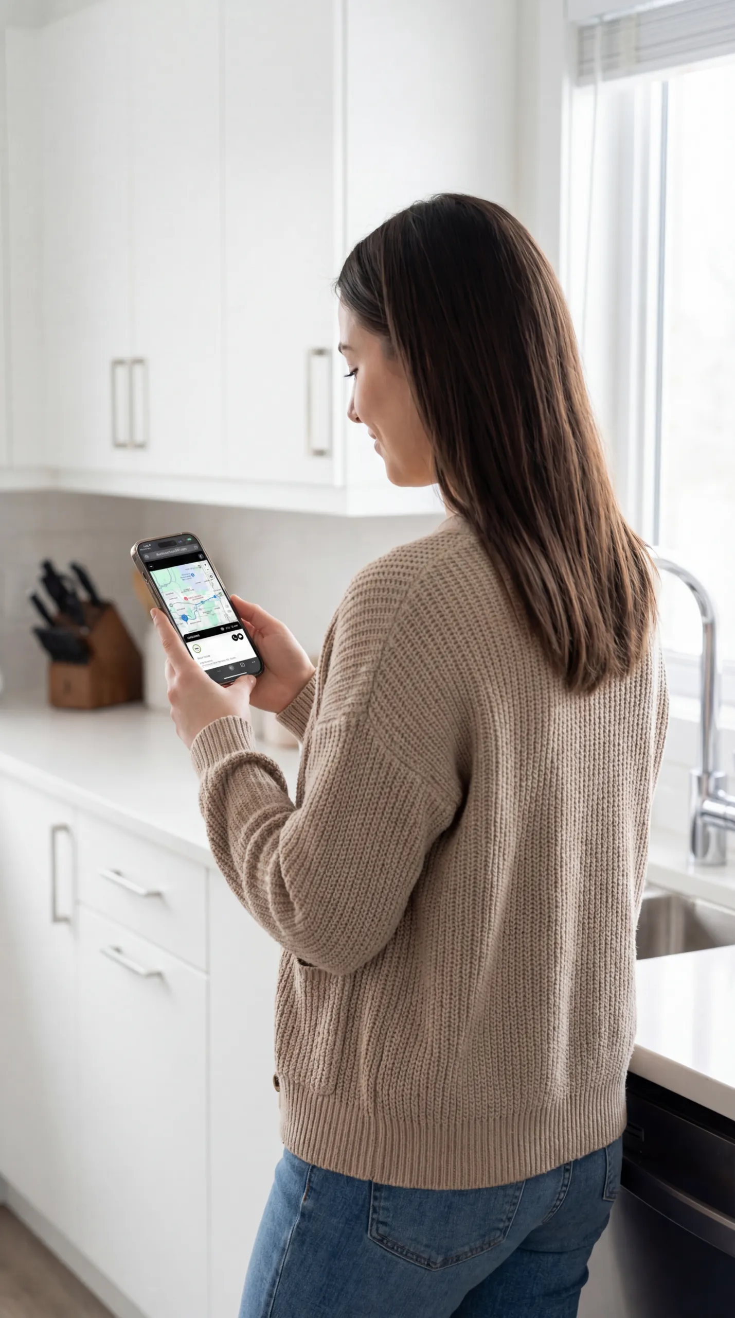 A woman in her kitchen looks at a live map on her phone while waiting for her technician to arrive.