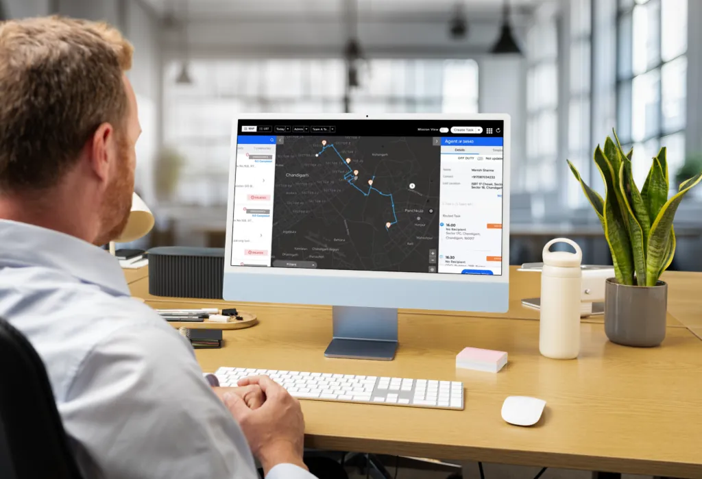 Dispatcher at a desk watching a monitor that shows a dark live map with technician routes and a job list