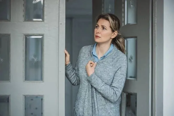 A woman stands at her front door, looking out anxiously for a service technician